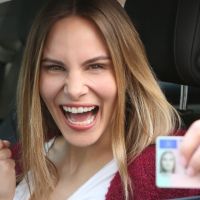 Junge Frau sitzt in ihrem Auto und zeigt ihren Führerschein.